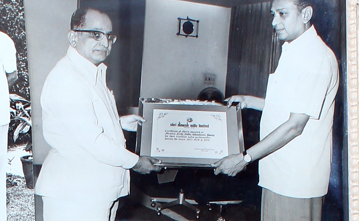Presentation of a framed Certificate of Merit between two men.